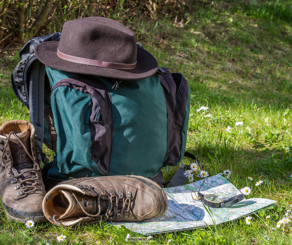 Wandern 🚶‍♂️ und zur Ruhe kommen: Entspannung und Naturerlebnis an den Pfingstfeiertagen. Finde tolle Wandertouren im Saarland oder im Drei Länder Eck. Auf dem Foto siehst du Wanderschuhe, einen Wanderrucksack, Kompass mit Karte, die auf einer Wiese mit Gänseblümchen (Bellis perennis)stehen.