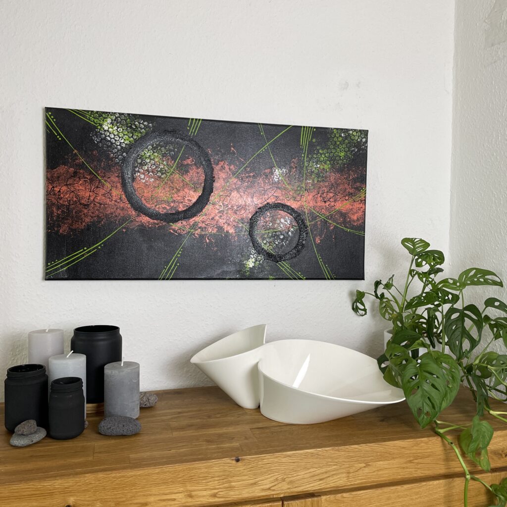 Abstraktes modernes Gemälde 40 cm x 80 cm mit schwarzen Kreisen und einem kupferfarbenem Streifen im Hintergrund. Das Acrylgemälde hängt über einem Sideboard auf dem eine weiße Schüssel, schwarze Gefäße, graue Kerzen und eine Grünpflanze stehen.