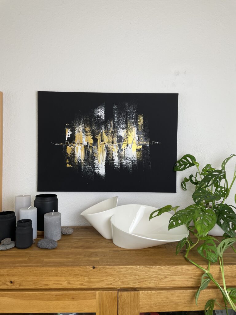 Das Schwarz, weiß und goldene Acrylgemälde auf Leinwand hängt im Wohnzimmer über dem Sideboard aus Holz.