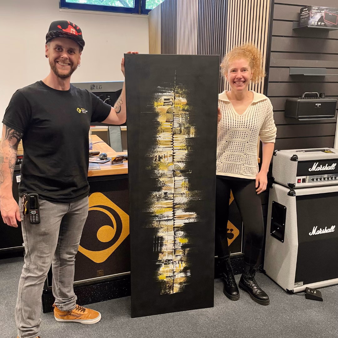 Die Auftragsarbeit von der deutschen Künstlerin Janiscolorart für das Musikcenter Saar in St. Ingbert. Auf dem Foto zu sehen sind der Geschäftsführer Kai Brömer und die Künstlerin Janina Feld, beide stehen neben dem 160 cm langen und 55 cm breiten Gemälde in Schwarz, Weiß und verschiedenen Goldtönen.