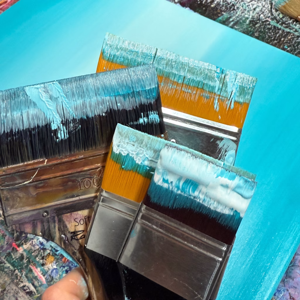 Mit blauer Farbe beschmierte Flachpinsel im Atelier der deutschen Künstlerin Janiscolorart.