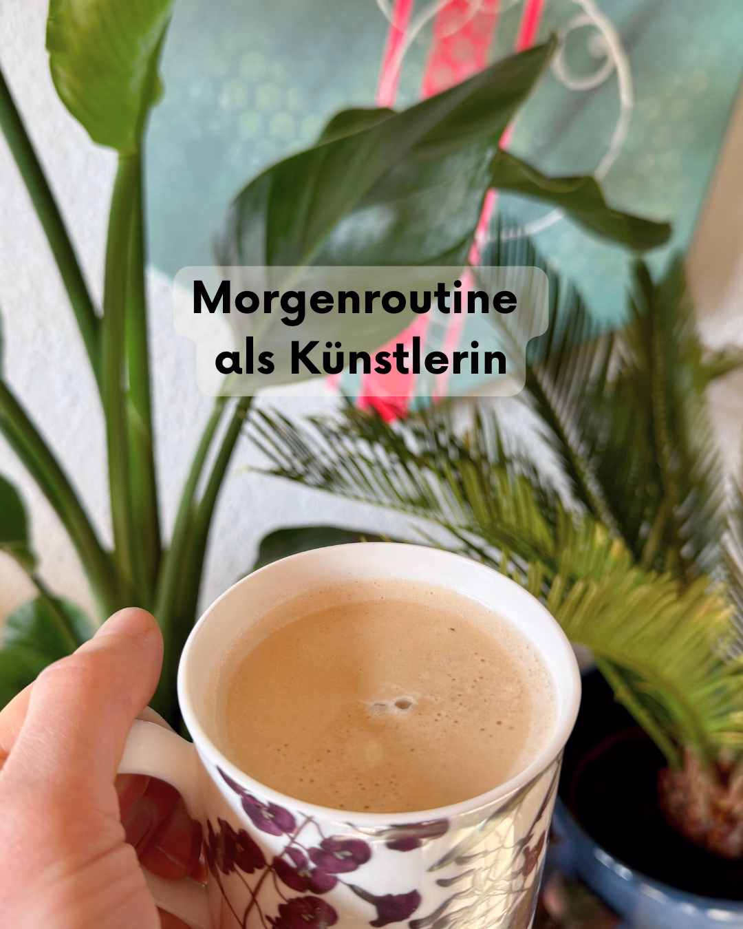 Morgenroutine als Künstlerin: Die Hand von Janina (Janiscolorart) hält eine Tasse Kaffee inmitten von grünen Zimmerpflanzen und Kunst. Ein persönlicher Einblick und Tipps für einen achtsamen und kreativen Start in den Tag von der Künstlerin aus dem Saarland.