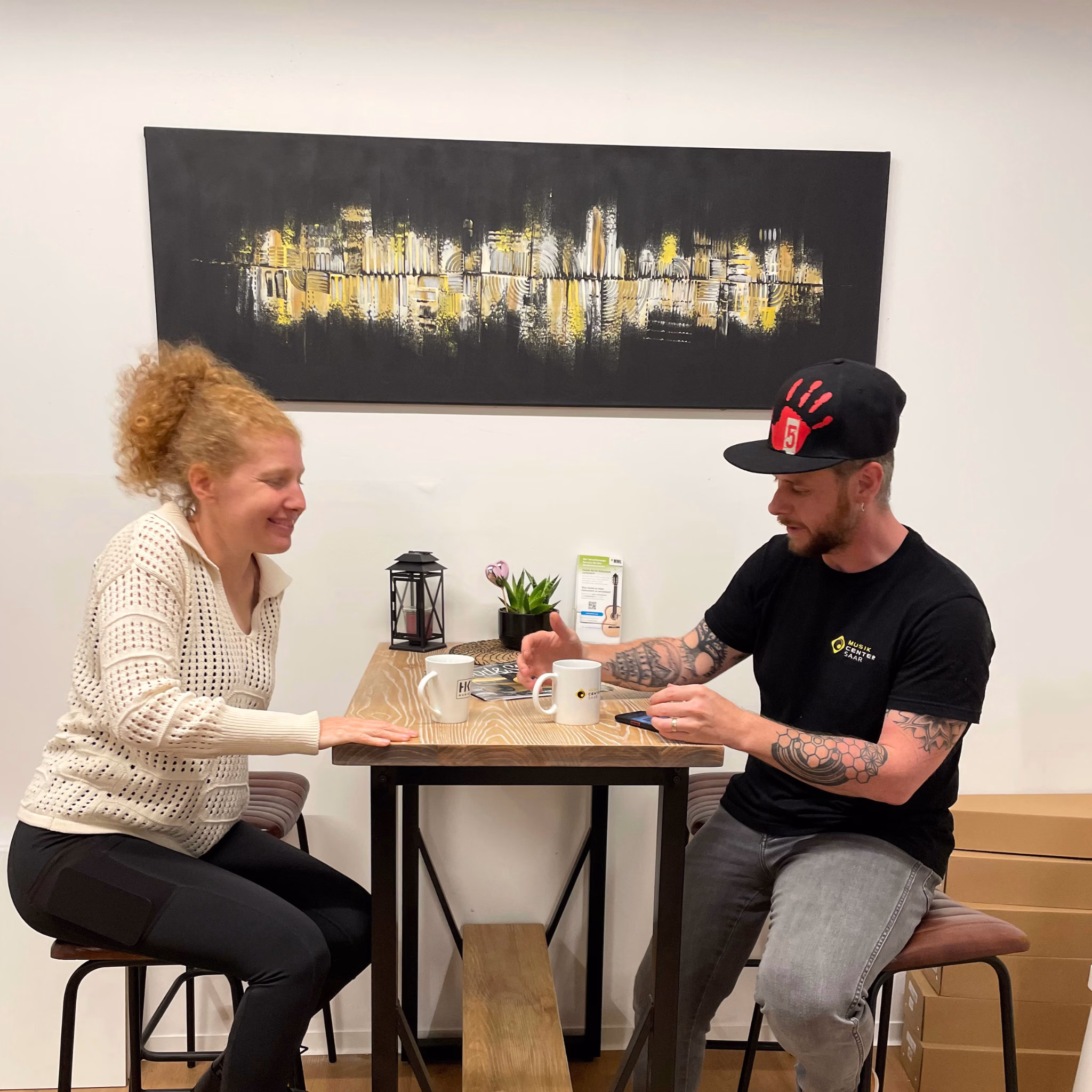 Künstlerin Janina Feld von Janiscolorart im Gespräch vor einem großen abstrakten Skyline-Gemälde in Schwarz und Gold.