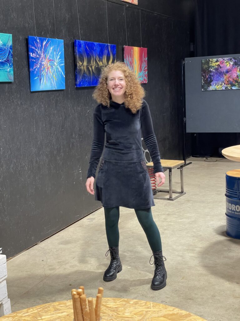 Vernissage in der Kreativwerkstatt Illingen mit der deutschen Künstlerin Janina Feld von Janiscolorart. Im Hintergrund sieht man ihre Gemälde. Eins davon ist hellblau, ein anderes ist Königsblau mit Schwarz und Gold.