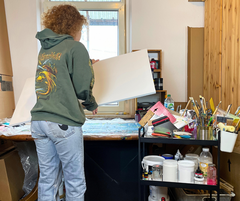 Die Künstlerin Janina Feld in ihrem Atelier bei Vorbereitungen zum Malen. Sie lebt im Saarland. Um genau zu sein in Neunkirchen Saar. Sie benutzt das abstrakte Malen auch zum Stressabbau. Janina trägt eine hellblaue Jeans und einen olivgrünen Kapuzenpulli mit Drachenaufdruck.