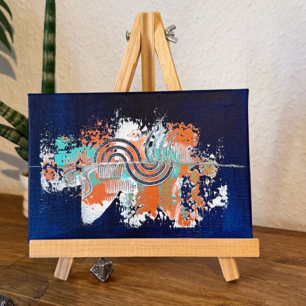 Kleines abstraktes Acrylbild der Künstlerin Janiscolorart in Dunkelblau, Orange und Türkis, präsentiert auf einer Mini-Staffelei auf einem Sideboard.