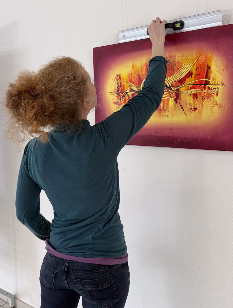 Die Künstlerin Janiscolorart beim Aufhängen eines ihrer abstrakten Kunstwerke.